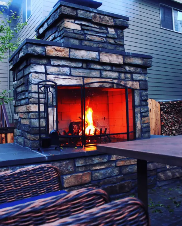 Custom outdoor stone fireplace with iron screen doors and seating area in West Linn OR – Oregon Quality Cuts